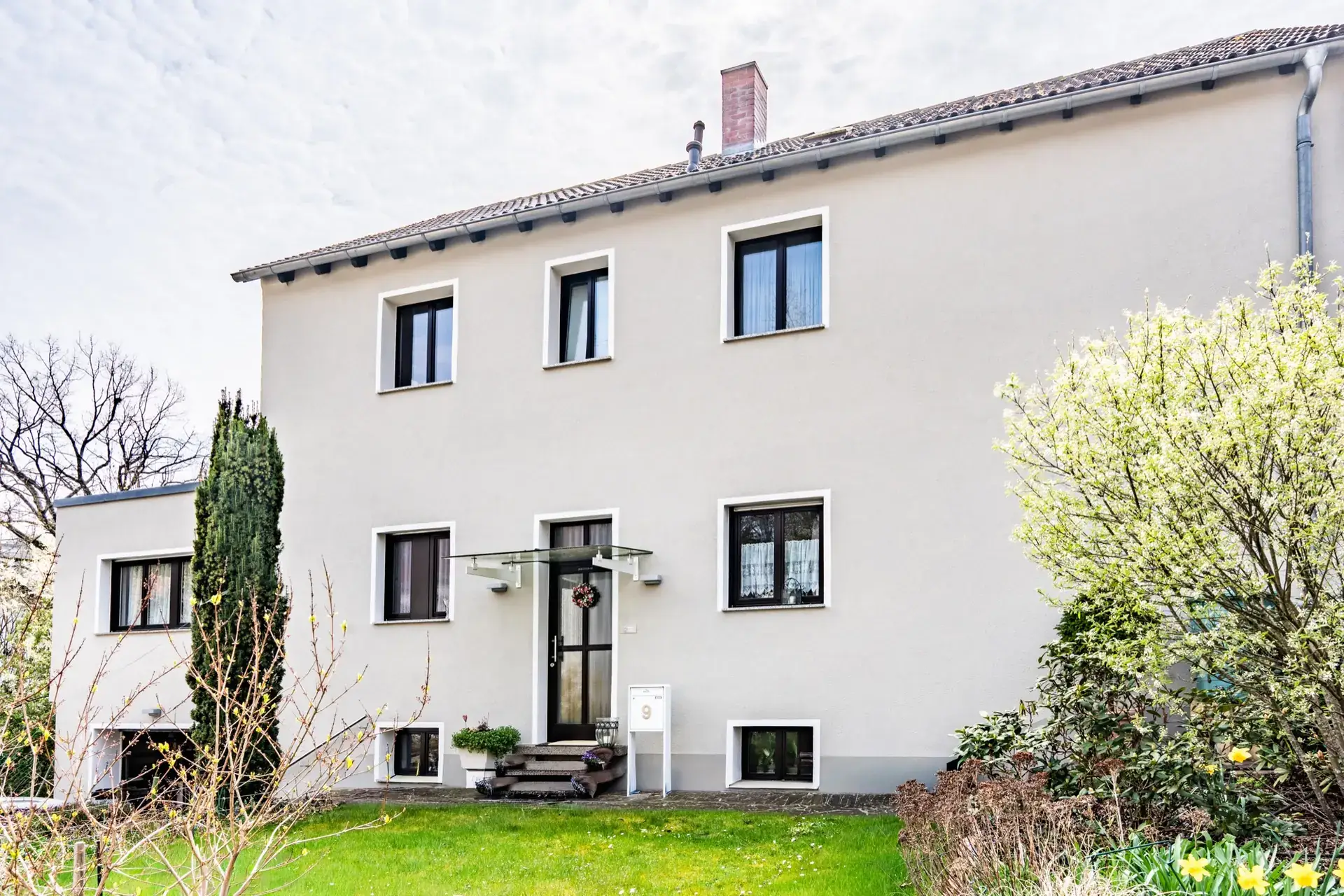 Zweistöckiges Wohnhaus mit hell gestrichener Fassade und Garten