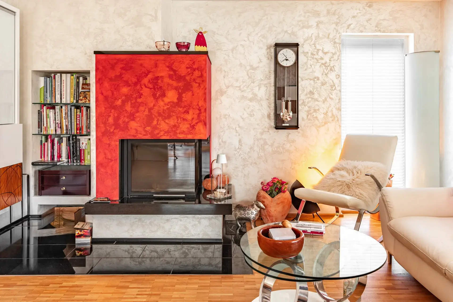 Wohnzimmer mit roter Kaminwand, Bücherregal und hellen Wänden
